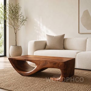 Può includere: Un tavolino da caffè in legno massello marrone scuro con un design curvo unico. Il tavolo ha una superficie liscia e lucida e un caratteristico ritaglio al centro. Il tavolo misura circa 122 cm di lunghezza e 51 cm di larghezza.