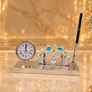 May include: A desk organiser set featuring a rectangular silver base, a round analogue clock with a gold rim and Roman numerals, a silver peacock figurine adorned with colourful crystal accents, and a black and silver pen in a vertical holder.