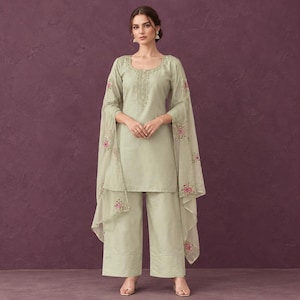 Könnte beinhalten: Ein helles salbeigrünes dreiteiliges Set, bestehend aus einer langärmeligen Tunika mit aufwendiger Stickerei am Ausschnitt, einer weiten Hose und einem transparenten, leichten Dupatta mit zarten rosa und grünen Blumenstickereien an den Rändern.