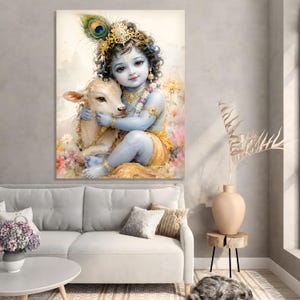 Könnte beinhalten: Gerahmter Kunstdruck eines blauhäutigen Kindes mit lockigem Haar, geschmückt mit Goldschmuck und einer Krone, das ein weißes Kalb umarmt. Das Kunstwerk zeigt eine Pfauenfeder und florale Akzente, vor einem weichen, aquarellartigen Hintergrund.