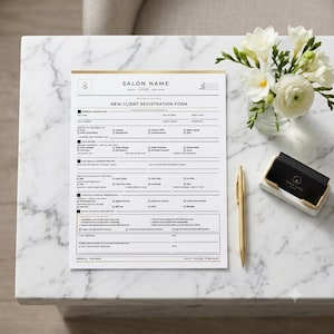 Op de afbeelding: Een wit papieren registratieformulier voor nieuwe salonklanten met zwarte tekst en gouden accenten. Het formulier bevat secties voor persoonlijke gegevens, haarhistorie, doelen en beleid. Een gouden pen en een zwarte visitekaartjeshouder liggen ernaast.