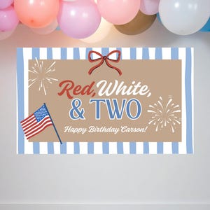 May include: A patriotic birthday banner with the text "Red, White, & TWO" in red and blue, with an American flag and fireworks illustrations. The banner has a tan background with a blue and white striped border, and a red bow at the top.