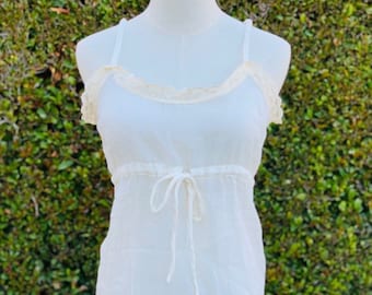 May include: A white sheer top with a lace trim and a tie at the waist.