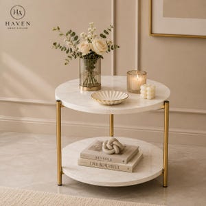 May include: A two-tier round side table with a white marble-patterned top and shelf supported by four gold-toned metal legs. The top shelf holds a ribbed glass vase with white flowers, a scalloped white dish, and a white candle. The bottom shelf holds two books.