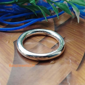 Op de afbeelding: Een gepolijste zilveren ring met een gladde, ronde band. De binnenkant van de ring is voorzien van een klein, gestempeld keurmerk met de tekst 925. Het metalen oppervlak is reflecterend en vangt het licht, met een eenvoudig rond ontwerp.