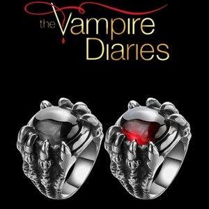 May include: Two silver rings with a claw design holding a large, round gemstone. One ring has a black gemstone, the other a red gemstone. The text "The Vampire Diaries" is above the rings.