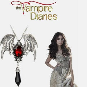 May include: Silver-toned pendant necklace with a large, oval, red gemstone and a black, pointed, teardrop-shaped stone. The pendant has wing-like details and is from "The Vampire Diaries".