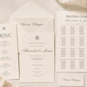 Op de afbeelding: Elegante trouwbriefpapier set op een crèmekleurige achtergrond. Inclusief een menu, uitnodiging, plattegrond, envelop en naamkaartje. De uitnodiging bevat de namen "Alexandra & James". Een zegel en bloemen maken het geheel af.