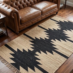 Könnte beinhalten: Rechteckiger Teppich mit einem geometrischen Muster in Schwarz und Beige. Der Teppich besteht aus Naturfasern und hat einen Fransenrand. Im Hintergrund befindet sich ein braunes Ledersofa.