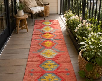 May include: A long, rectangular runner rug featuring a vibrant coral-orange base colour. The rug is decorated with a repeating geometric pattern consisting of large, centred yellow diamonds surrounded by grey diamond outlines and red jagged accents.