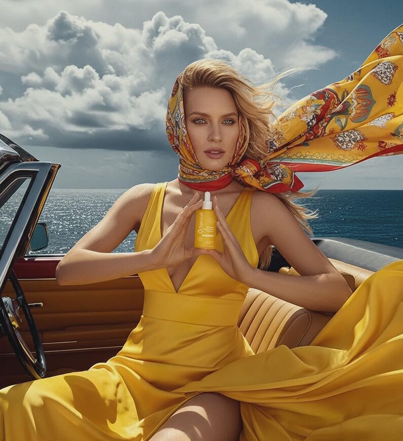 May include: A woman in a yellow dress and headscarf holds a yellow bottle with a white dropper. The woman is seated in a vintage convertible with the ocean and sky in the background. The headscarf is yellow with a red and patterned design.