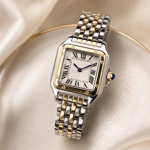 May include: A two-tone silver and gold wristwatch with a square face and a white dial. The watch features black Roman numerals and blue hands. The gold-toned watch case has a blue gemstone on the side.