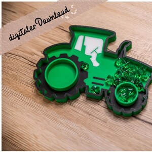 May include: A green and black tractor-shaped tray with a white cabin window detail. The tray features two circular recessed areas, one of which is filled with small, translucent green acrylic gems, while additional green gems are scattered nearby.