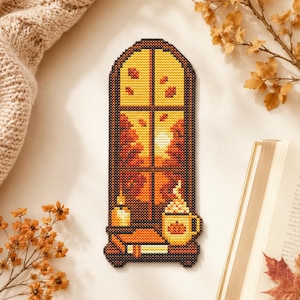 Può includere: Un motivo a punto croce raffigurante una finestra ad arco con vista su alberi autunnali e foglie cadenti. Sul davanzale si trovano una candela accesa, una pila di libri e una tazza con un disegno di zucca e panna, in stile pixel.