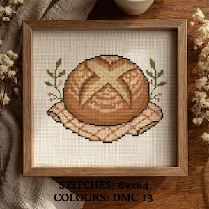 Pode incluir: Uma bordado em ponto cruz emoldurado de um pão, com um design detalhado com uma cruz no topo. O pão está sobre um pano xadrez, rodeado por folhas verdes e bagas vermelhas. O texto na parte inferior diz "STITCHES: 89x64 COLOURS: DMC 13".