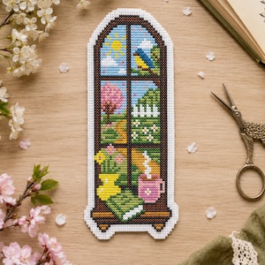 May include: A rectangular cross-stitch bookmark featuring an arched window design. The scene depicts a sunny outdoor landscape with a blue bird, a pink tree, a white fence, and flowers. Inside, a yellow vase with flowers, a green book, and a pink mug.