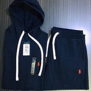 Pu&ograve; includere: Tuta blu navy con cappuccio e coulisse bianche. La felpa con cappuccio e i pantaloni della tuta coordinati presentano un logo arancione. Il completo &egrave; realizzato in materiale morbido.