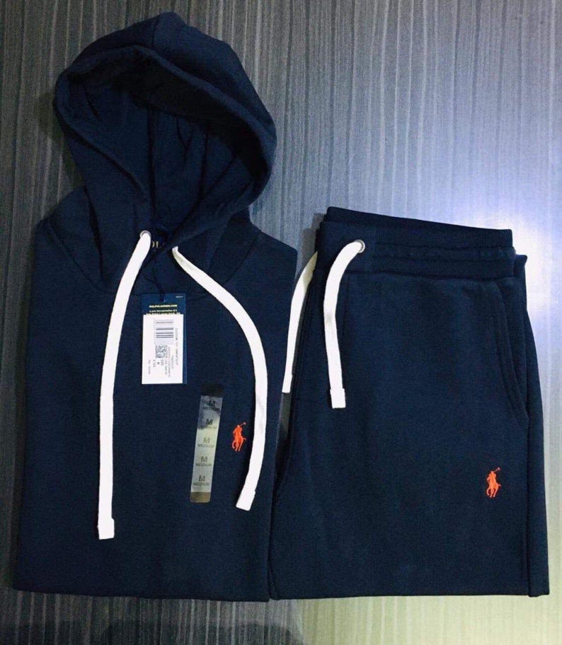 Pu&ograve; includere: Tuta blu navy con cappuccio e coulisse bianche. La felpa con cappuccio e i pantaloni della tuta coordinati presentano un logo arancione. Il completo &egrave; realizzato in materiale morbido.