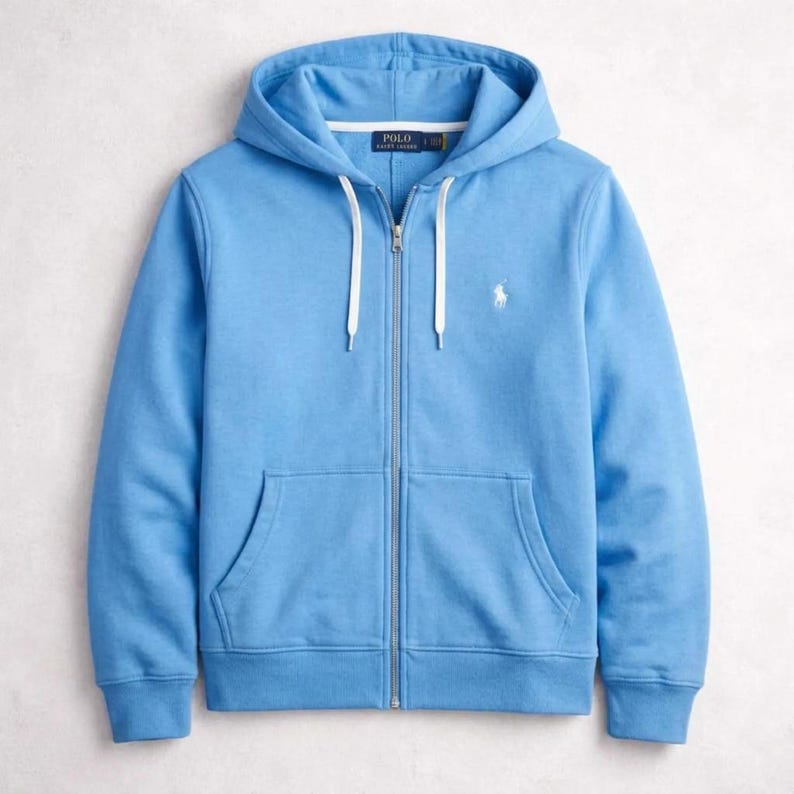 May include: A light blue zip-up hoodie with a drawstring hood and a kangaroo pocket. The hoodie features a white embroidered logo on the chest and a white zipper. The garment is made of a soft, comfortable material.