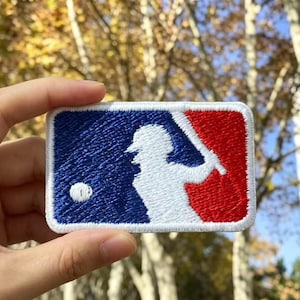 Może przedstawiać: Prostokątna haftowana naszywka z logo Major League Baseball. Wzór przedstawia białą sylwetkę baseballisty zamachującego się kijem, umieszczoną na niebieskim tle po lewej stronie oraz czerwonym tle po prawej stronie naszywki.