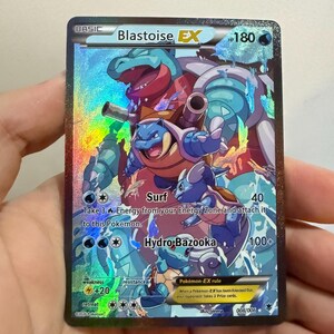 May include: A holographic Blastoise EX trading card featuring a large blue Blastoise, a Wartortle, and a Squirtle surrounded by water effects. The card displays 180 HP, Surf and Hydro Bazooka attacks, and the text 008/006 at the bottom.