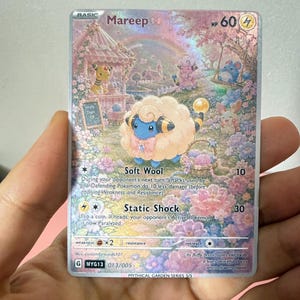 May include: A Mareep trading card with a holographic finish, featuring a blue and cream-coloured creature in a pastel floral garden. The card displays the text Mareep, HP 60, Soft Wool, and Static Shock, along with various game statistics and illustrations.