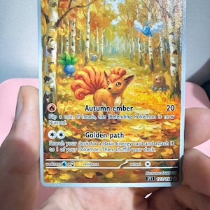 May include: A Vulpix trading card featuring a golden-brown fox-like creature in an autumn forest setting. The card displays 60 HP, the Autumn ember attack, and the Golden path ability. Other small creatures are visible in the background trees.