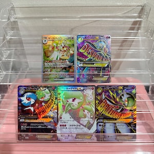 May include: Five Japanese Pokémon trading cards featuring Gardevoir and Mega Gardevoir characters. The cards display colorful illustrations, holographic foil textures, Japanese text, and various attack statistics, arranged in two rows on a clear stand.
