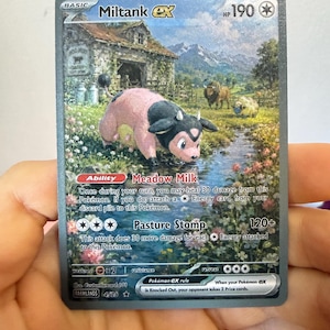 Könnte beinhalten: Eine Miltank EX Sammelkarte mit einem rosa-schwarzen, kuhähnlichen Wesen in einem Bach. Der Hintergrund zeigt eine rustikale Scheune, Berge und ein Feld mit anderen Tieren. Der Kartentext enthält die Fähigkeit Meadow Milk und den Angriff Pasture Stomp.