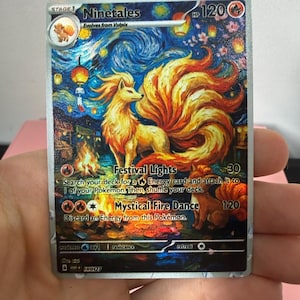 May include: A Ninetales trading card featuring a stylised illustration of the fox-like creature with nine tails, surrounded by a starry night sky, floating lanterns, and a campfire. The card displays the text Ninetales, Festival Lights, and Mystical Fire Dance with 120 HP.