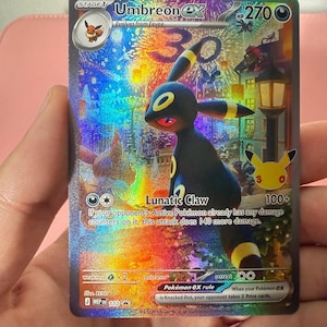 Op de afbeelding: Een holografische Umbreon ex ruilkaart met een donker wezen met gele ringen, rode ogen en de Lunatic Claw aanval. De kaart toont 270 HP, een 30-jarig jubileumlogo en een feestelijke nachtscène met vuurwerk en een lantaarnpaal.
