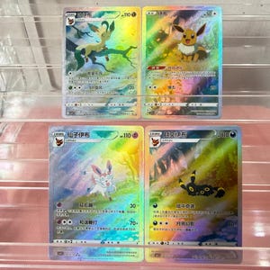 May include: Four holographic Pokémon trading cards featuring Leafeon, Eevee, Sylveon, and Umbreon. Each card displays colorful, reflective artwork with Chinese text, character names, HP values, and attack statistics printed on the surface.