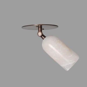 May include: A ceiling-mounted spotlight featuring a circular bronze-toned base and a cylindrical, translucent white stone shade. The fixture includes an adjustable swivel joint that connects the base to the stone housing, allowing for directional light.