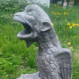 May include: A gray stone gargoyle statue with wings, perched on a stone base. The gargoyle has a wide open mouth and appears to be roaring.