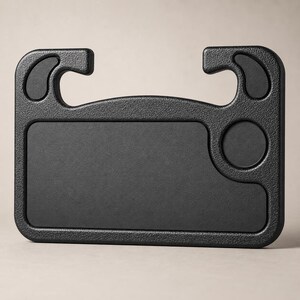 Puede incluir: Un escritorio negro de plástico moldeado para volante de coche. Cuenta con una superficie rectangular, un portavasos circular y dos ganchos curvos para la fijación. Diseñado para encajar sobre un volante.