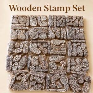 Op de afbeelding: Een verzameling houten stempels met ingewikkelde witte ontwerpen, waaronder paisley, bloemen en geometrische patronen. De stempels zijn verpakt in doorzichtig plastic. De tekst "Wooden Stamp Set" staat bovenaan.