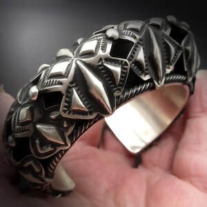 May include: A silver bracelet with a detailed geometric design. The bracelet is made of sterling silver and has a polished finish.