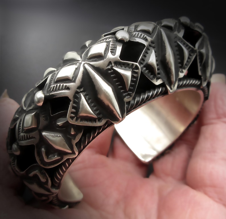 May include: A silver bracelet with a detailed geometric design. The bracelet is made of sterling silver and has a polished finish.