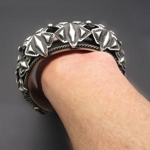 May include: A silver bracelet with a geometric design. The bracelet is made of multiple pieces that are connected together to form a continuous band. The design is intricate and detailed, and the bracelet is a statement piece.
