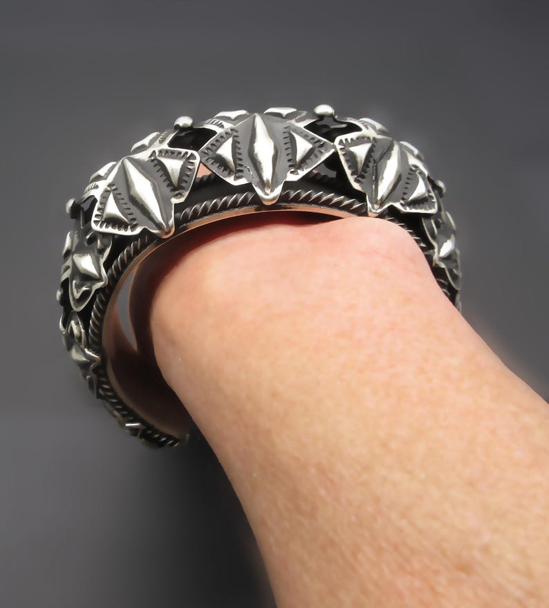 May include: A silver bracelet with a geometric design. The bracelet is made of multiple pieces that are connected together to form a continuous band. The design is intricate and detailed, and the bracelet is a statement piece.