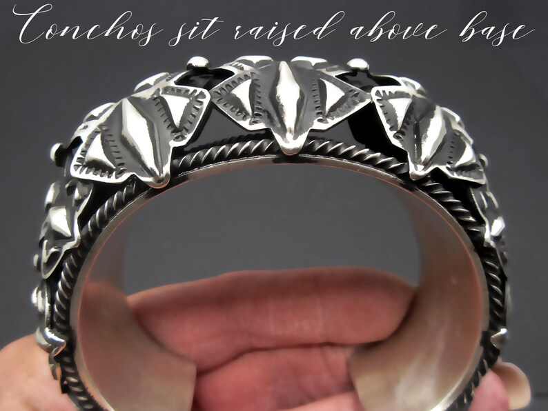 May include: Silver bracelet with a decorative design of raised conchos. The conchos are shaped like leaves and have a textured surface. "Conchos sit raised above base" is written on the top of the image.