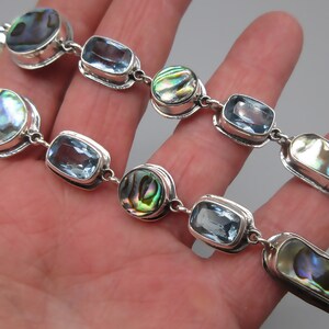 May include: A silver chain bracelet with alternating blue topaz and abalone shell beads. The bracelet is made of sterling silver and features a polished finish.