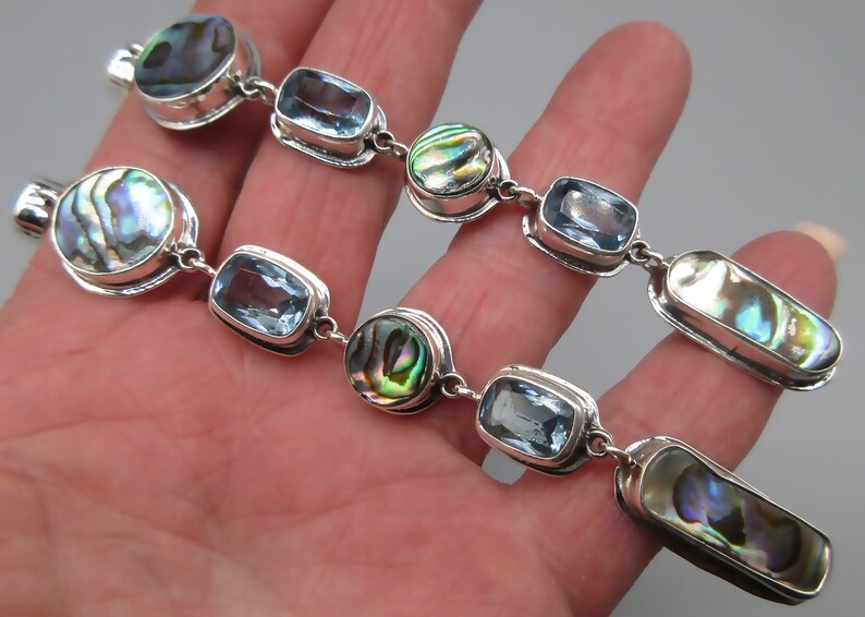 May include: A silver chain bracelet with alternating blue topaz and abalone shell beads. The bracelet is made of sterling silver and features a polished finish.