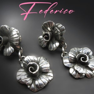May include: Silver-toned floral earrings with a layered petal design and a dangling flower. The earrings have a textured finish and are connected by small chains. The word "Federico" is written in pink script at the top.