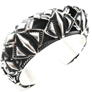May include: A silver cuff bracelet with a geometric design. The bracelet is made of metal and has a textured surface.