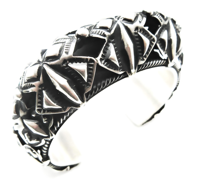 May include: A silver cuff bracelet with a geometric design. The bracelet is made of metal and has a textured surface.
