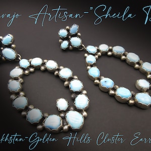 May include: A pair of silver earrings with turquoise stones. The earrings are in the shape of a circle with a cluster of turquoise stones in the center. The earrings are labeled "Navajo Artisan - Sheila Tso" and "Kazakhstan - Golden Hills Cluster Earrings".