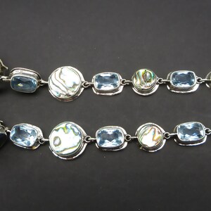 May include: A pair of long silver clip-on earrings with blue topaz and abalone shell accents.