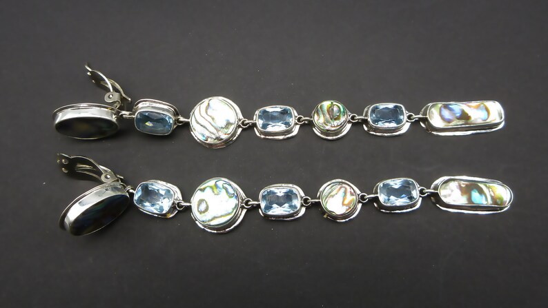 May include: A pair of long silver clip-on earrings with blue topaz and abalone shell accents.