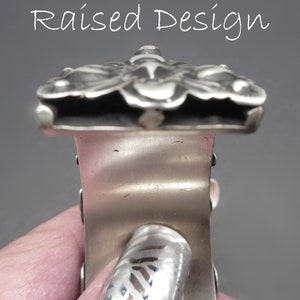 May include: A silver bracelet with a raised design of a butterfly. The bracelet is made of metal and has a polished finish.